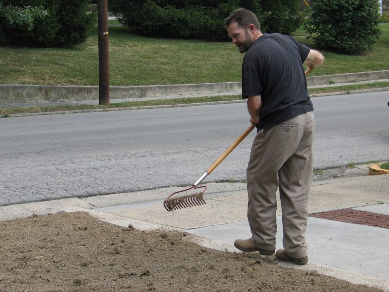 Man prepping soil with rake for seeding a lawn
